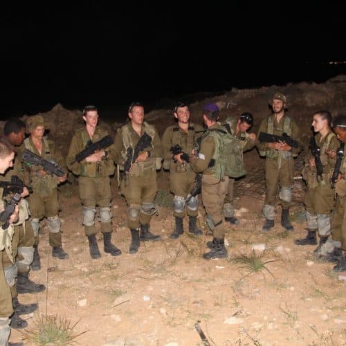 קבוצת חיילים עם נשק עומדת בחצי מעגל בשטח פתוח בלילה