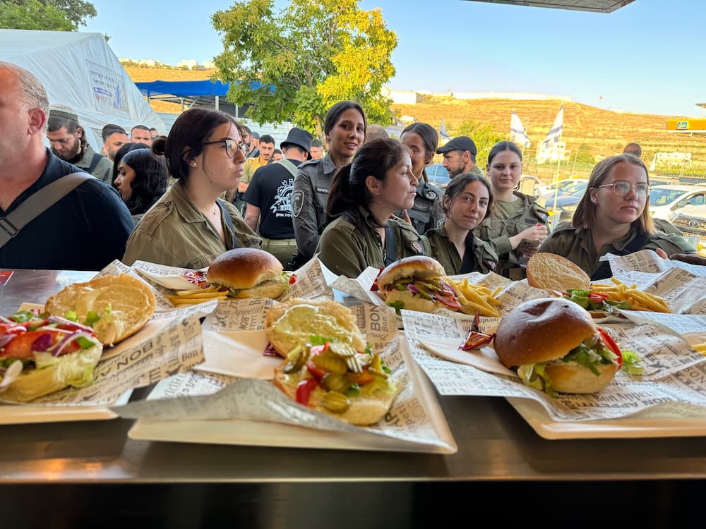 חיילות וחיילים עומדים בתור מול שורת מגשים עם המבורגרים וצ׳יפס