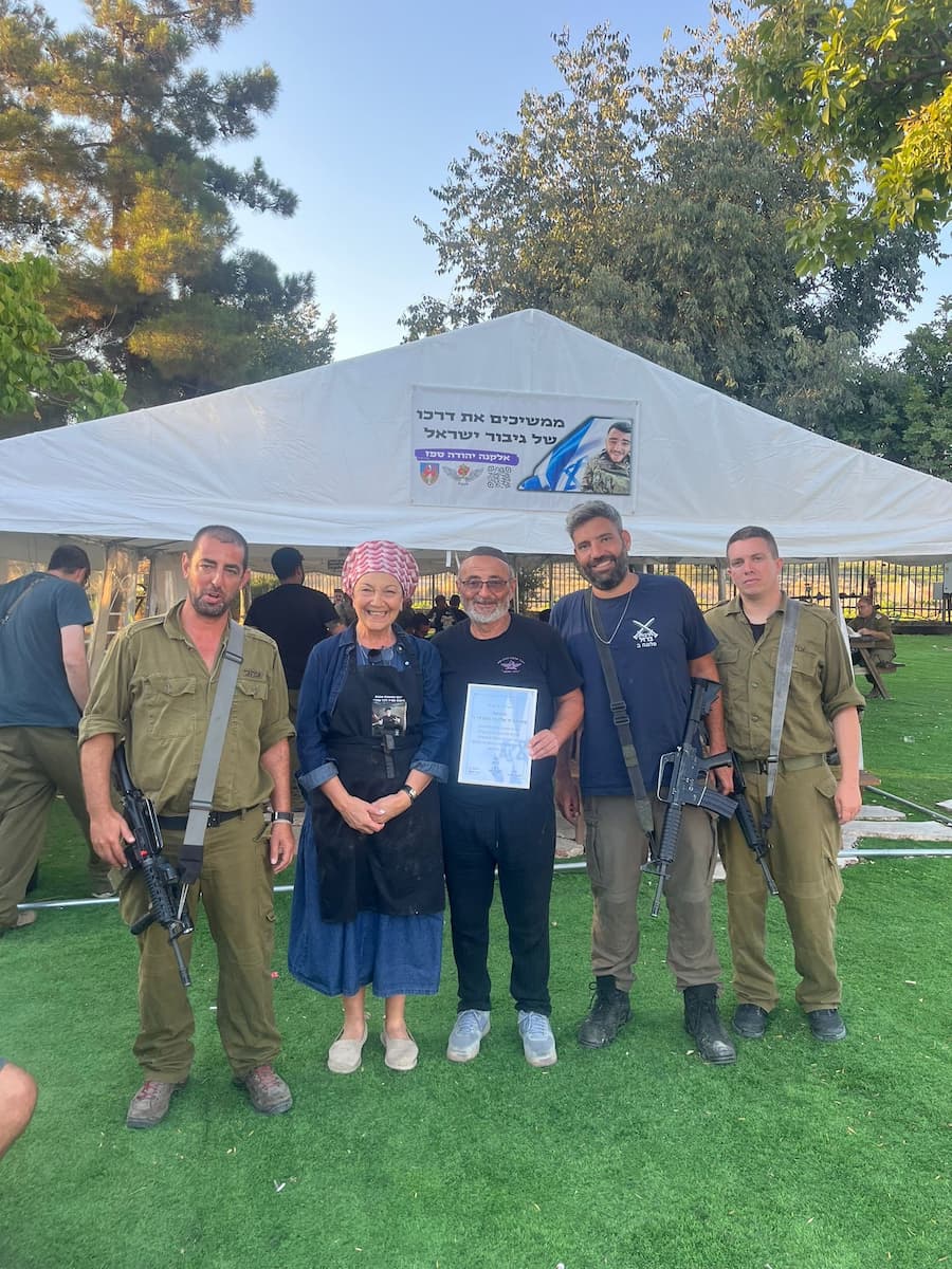 חמישה אנשים עומדים על הדשא מול אוהל לבן, ביניהם שלושה חיילים; אחד האזרחים מחזיק תעודה