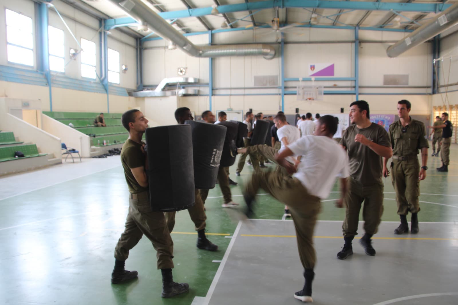 חיילים באימון קרב מגע באולם ספורט: אחד בועט במגן שמחזיק חברו
