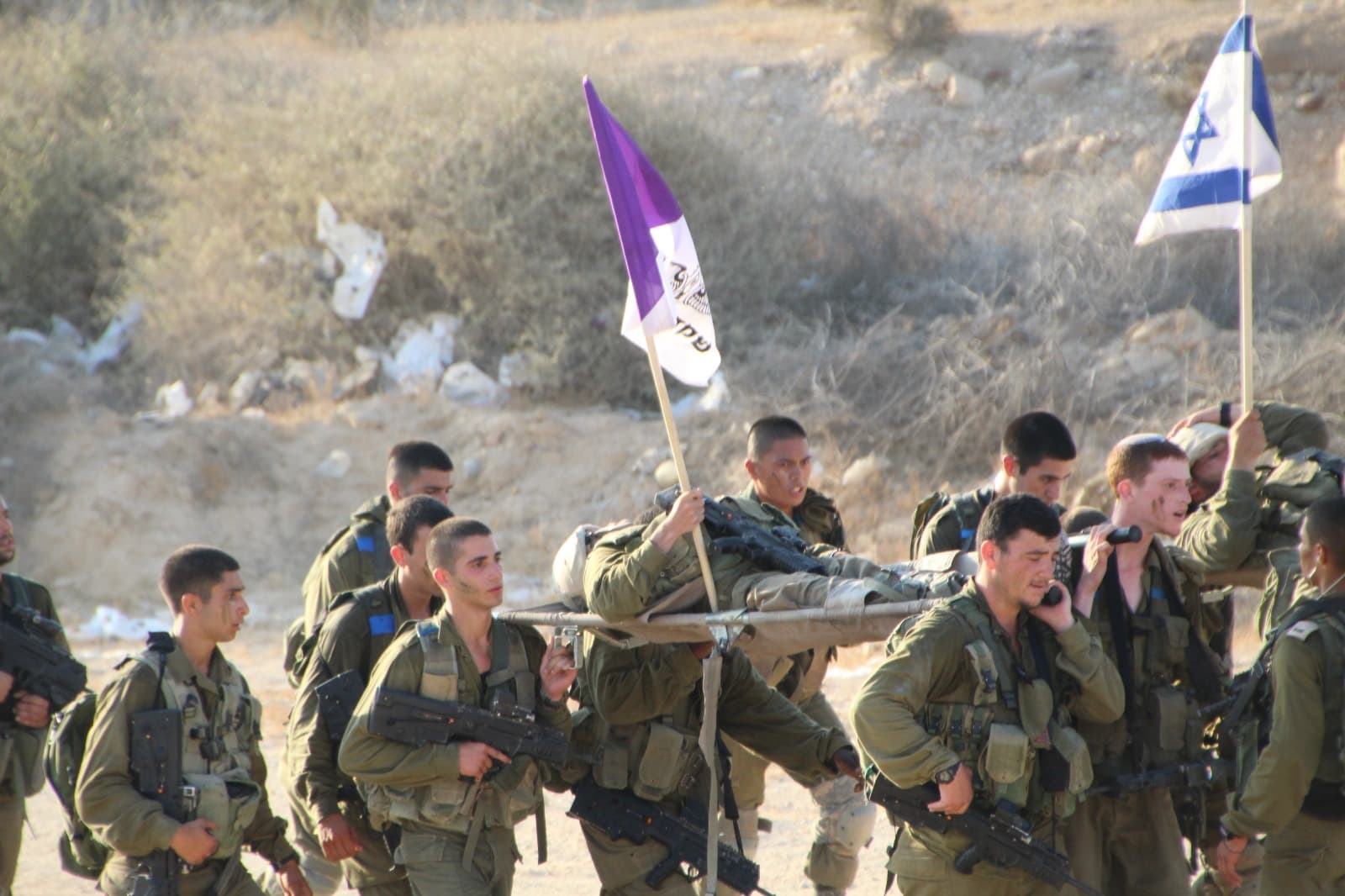 חיילים נושאים אלונקה במסע, ומעליהם מתנוססים דגל סגול של גבעתי ודגל ישראל