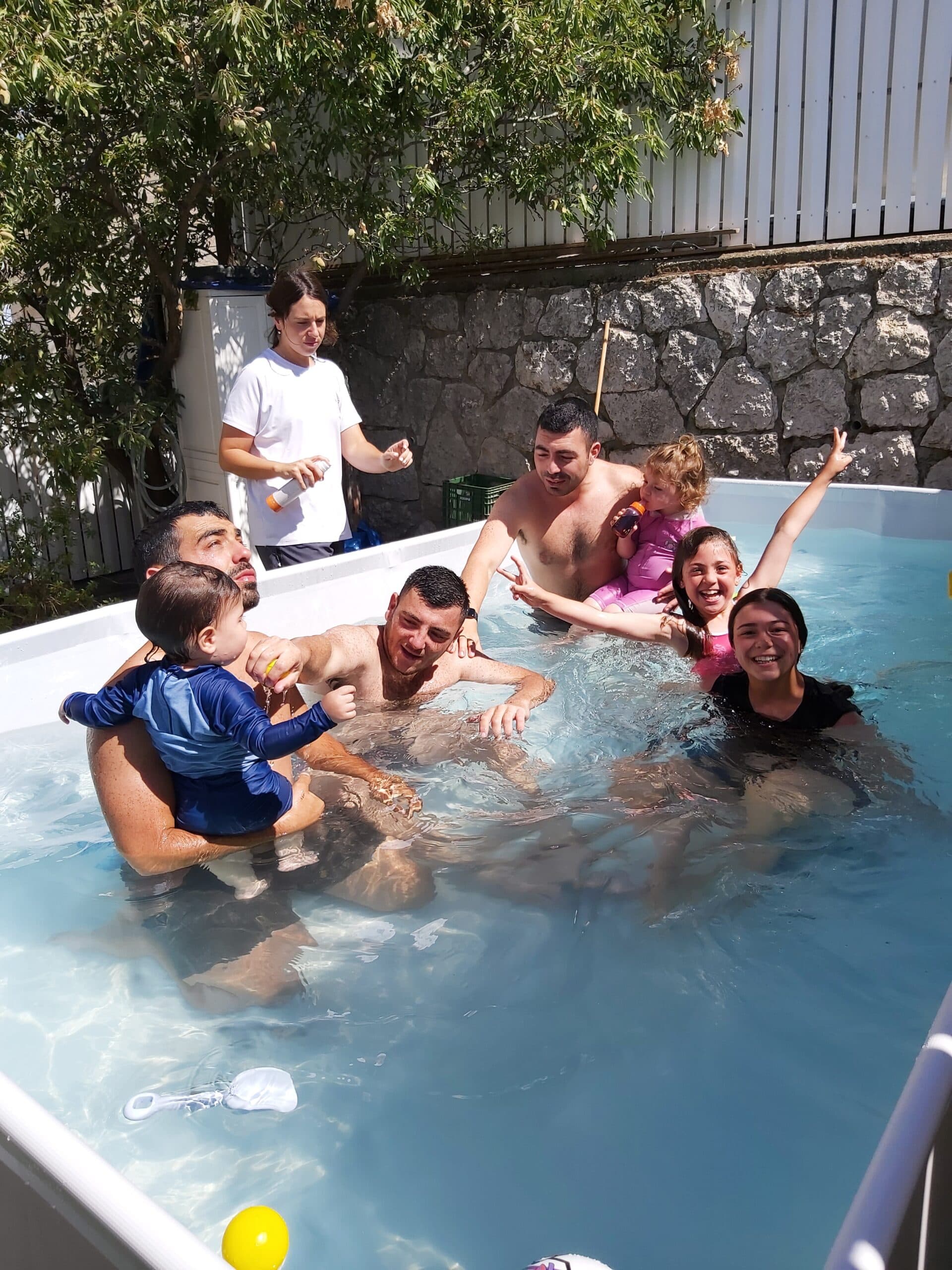 קבוצת צעירים וילדים משתעשעים יחד בבריכה בחצר