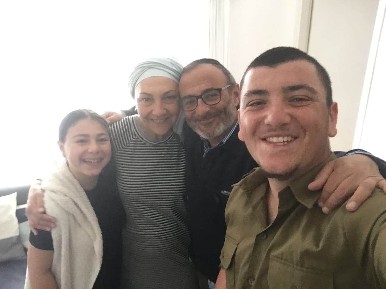 אלקנה במדים מצלם סלפי ומחייך, ולצידו נערה, אישה וגבר מחובקים