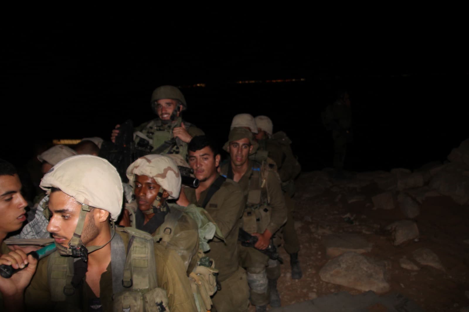 חיילים עם קסדות יושבים צמודים זה לזה בלילה