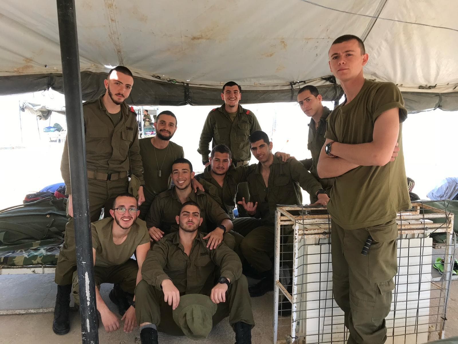 קבוצת חיילים מחייכת מתחת לסככה, חלקם יושבים וחלקם עומדים