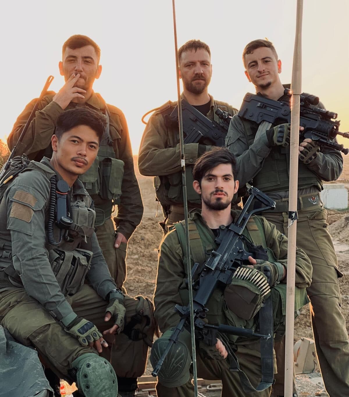 חמישה חיילים בציוד קרבי מלא מצטלמים יחד בשטח לעת ערב